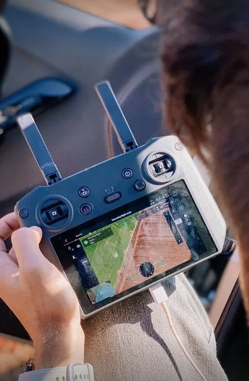 Profissional da equipe operando o controle de um drone, com a ortofoto do terreno na tela.